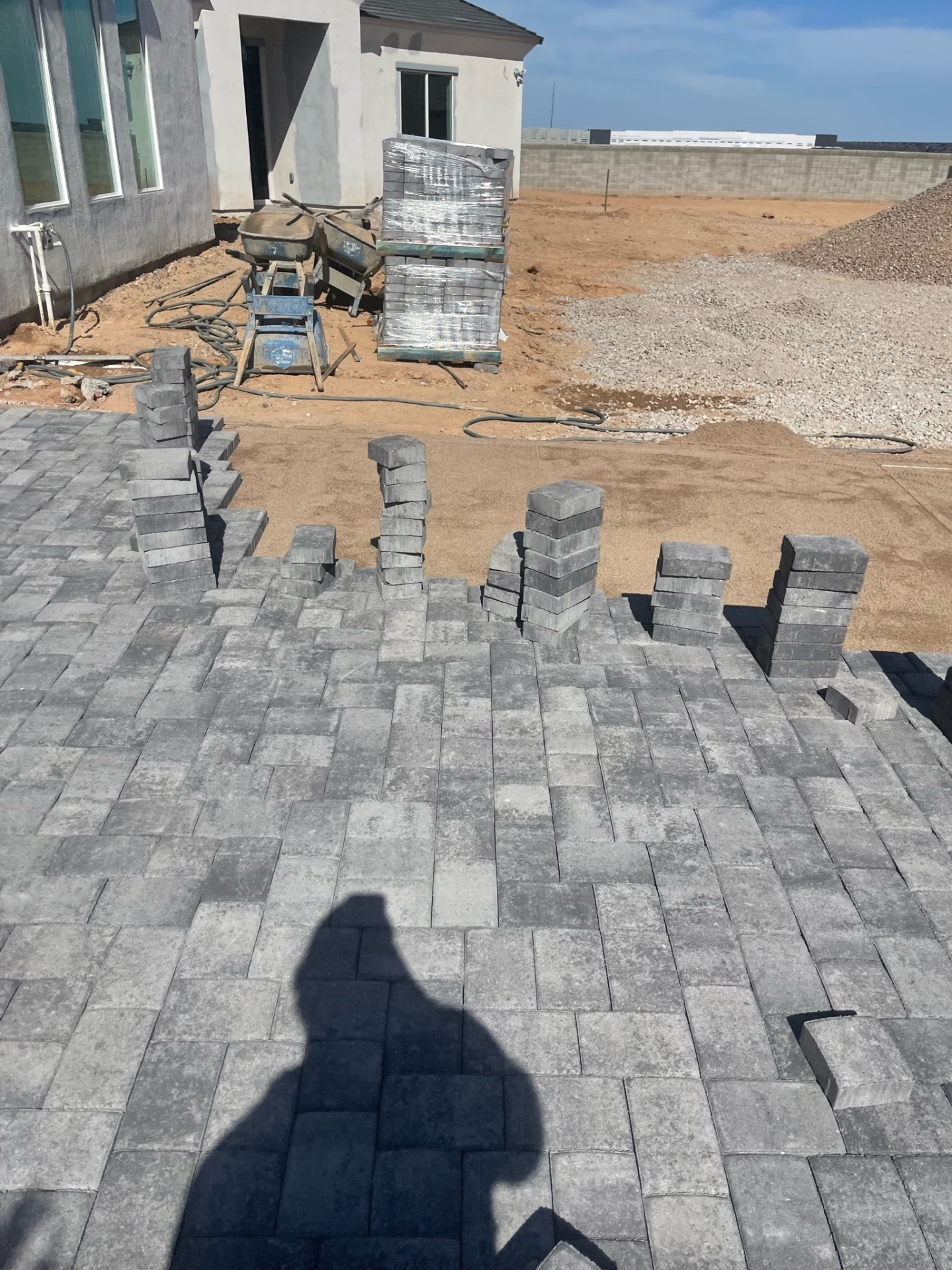 Waddell (Surprise-area) rear paver patio install with stacked charcoal paver bundles positioned across screeded sand base for continuous production by AE Outdoor Living
