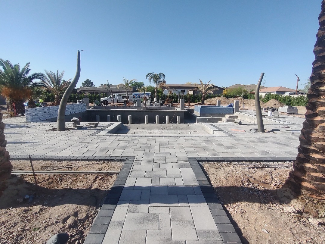 Wide view of finished paver deck around a pool and spa shell with newly set palm trees