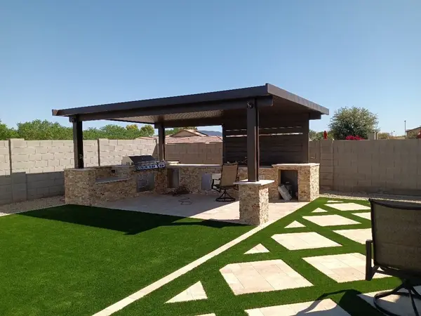 Outdoor kitchen under a pergola with turf and patterned hardscape tying the whole yard together.