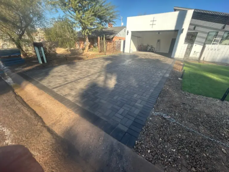 Same charcoal paver driveway seen from the street with lit address marker and turf apron.