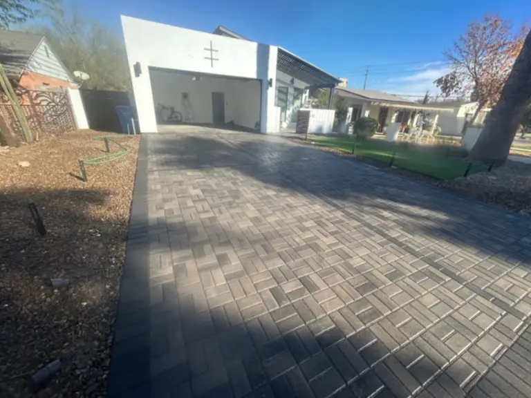 Charcoal paver driveway with sailor-course border serving a modern white stucco home.