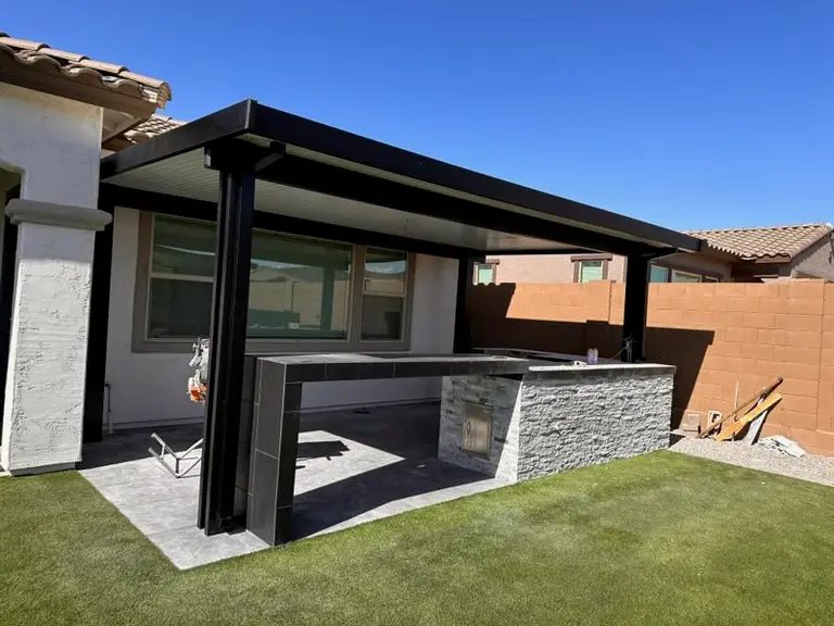 Blackout aluminum patio cover shading a stacked-stone outdoor kitchen and porcelain-tile counters.