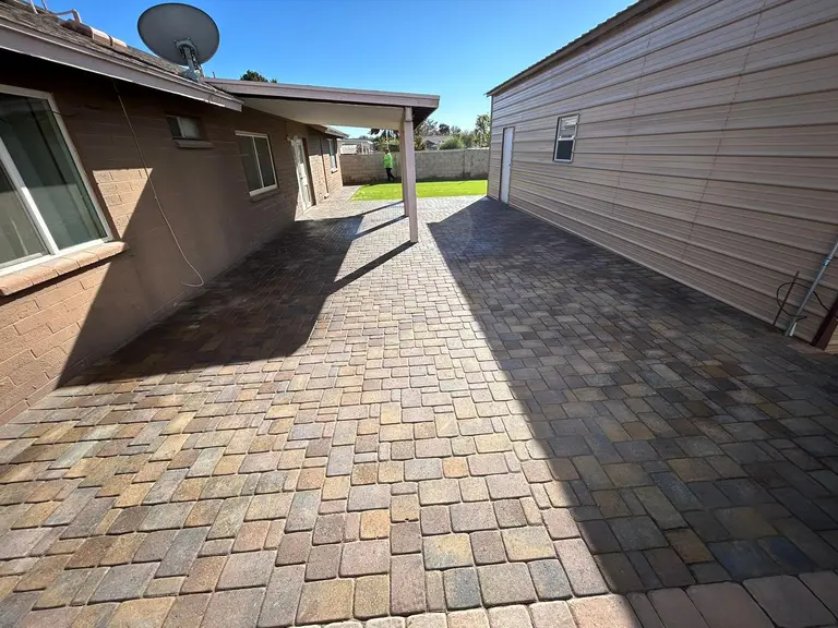 Full tumbled paver patio wrapping the back of the house toward the turf lawn.