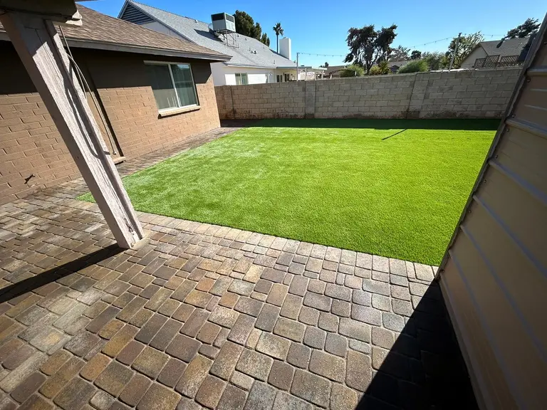 Tumbled paver patio meeting a fresh turf lawn under a covered back porch.